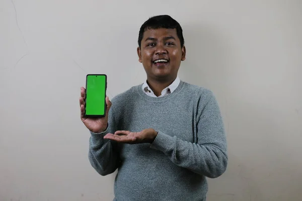 Akıllı telefonu sağ elinde tutan Asyalı bir adam gülümserken akıllı telefon ekranını gösteriyor, yeşil akıllı telefon ekranını gösteriyor.
