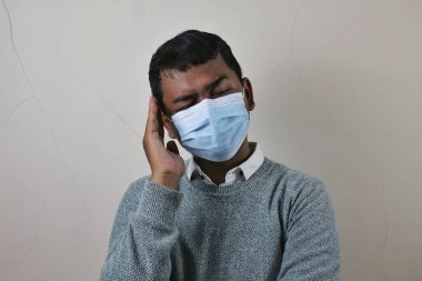 a young asian man wearing a medical mask holding his head it hurts or is having a headache