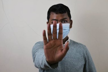 Tıbbi maske takan genç bir Asyalı durdurma hareketi sergiliyor, virüsün yayılmasını engelliyor ve sağlık protokollerine uyuyor.