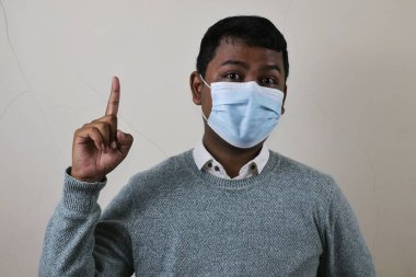 Koronavirüs koruması ve reklamı için sağ elinin işaret parmağıyla işaret eden tıbbi maske takan genç bir Asyalı.