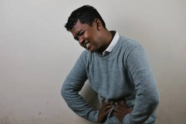 両手で胃を抱え痛みを伴う表情を見せるアジア系の青年 — ストック写真