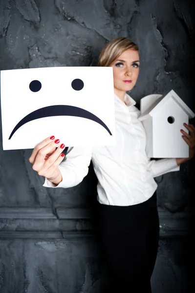 Die junge Geschäftsfrau in einem Arm hält das Haus, und in einem anderen traurigen Lächeln — Stockfoto