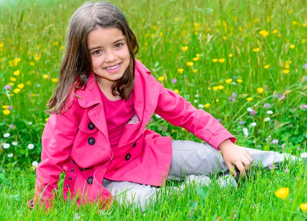 Glad söt barn sitter i en gräset på en blomma trädgård — Stockfoto