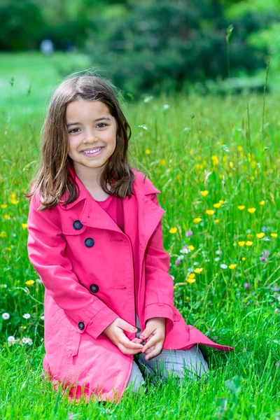 Glückliches süßes Kind sitzt in einem Blumengarten — Stockfoto