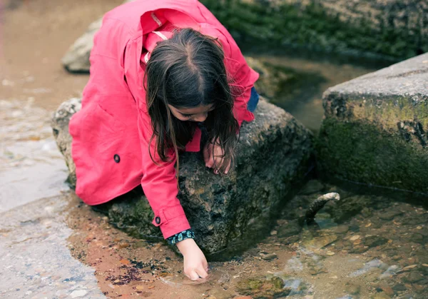 Bonita niña jugando en una roca en el borde del agua — Foto de Stock