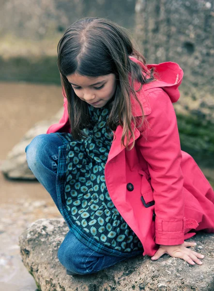 Bonita niña jugando en una roca en el borde del agua —  Fotos de Stock