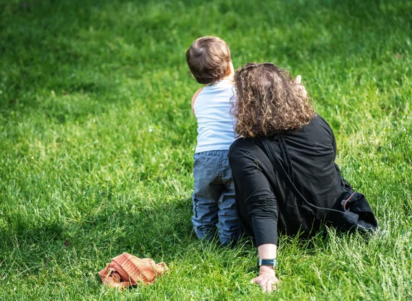 Donna seduta sull'erba che indica qualcosa al suo giovanissimo figlio in piedi accanto a lei — Foto Stock