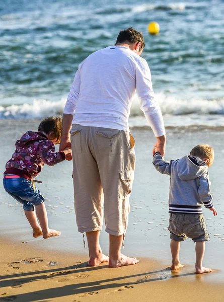 Duas crianças e seu pai brincando em frente ao oceano — Fotografia de Stock