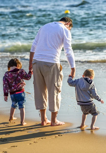 Двое детей и их отец играют на берегу океана — стоковое фото