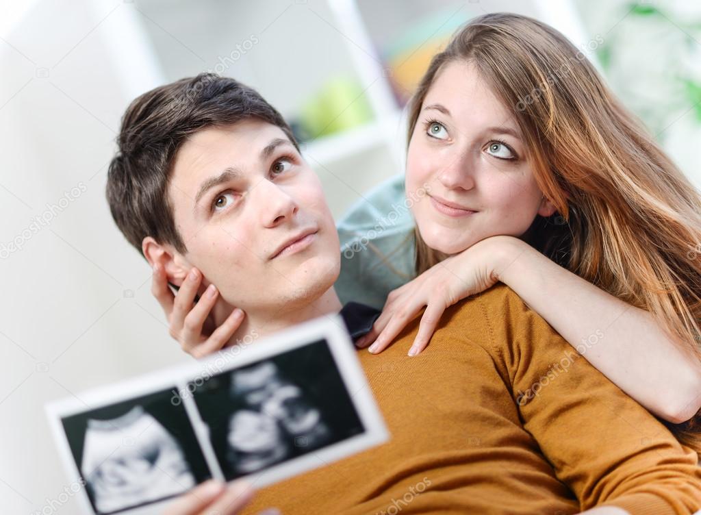 Beautiful couple imagines the future of their unborn child with ultrasound pictures in hands