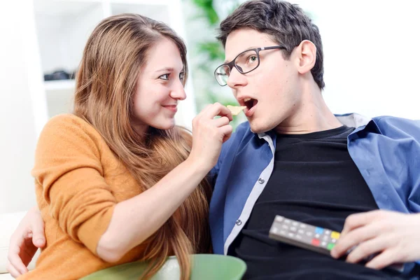 Beautiful young woman giving food to her darling front of the TV — Stock Photo, Image