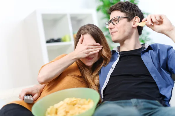 Amantes bonitos comendo e assistindo a um filme de terror ou violento — Fotografia de Stock