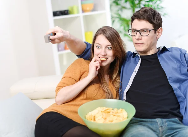 Muy linda pareja joven comiendo y viendo la televisión en un sofá — Foto de Stock