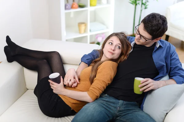 Attractive couple of lovers sitting on a sofa taking a hot drink — Stock Photo, Image