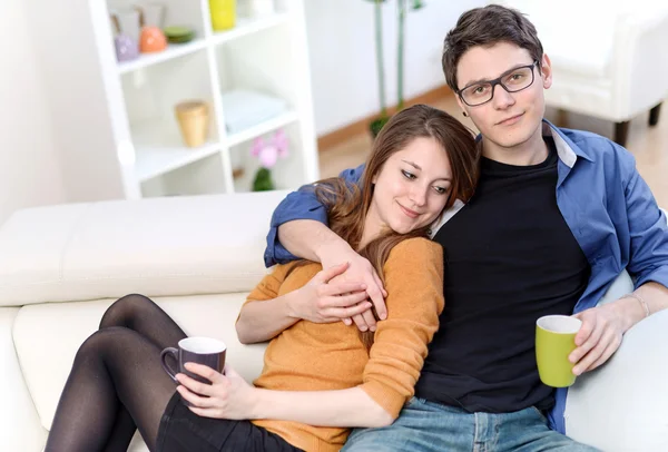 Atractiva pareja de amantes sentados en un sofá tomando una bebida caliente — Foto de Stock