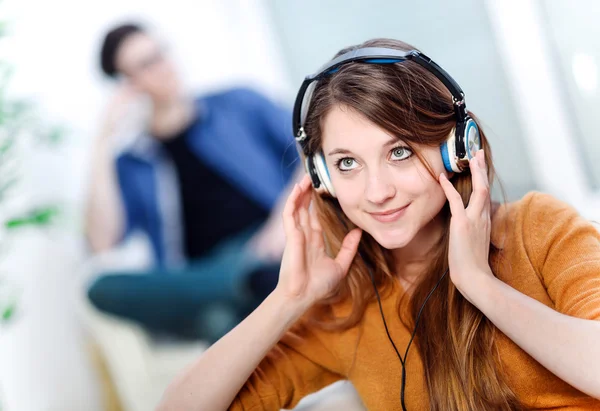 Beautiful blond listening to some music while her boyfriend is bored — Stock Photo, Image