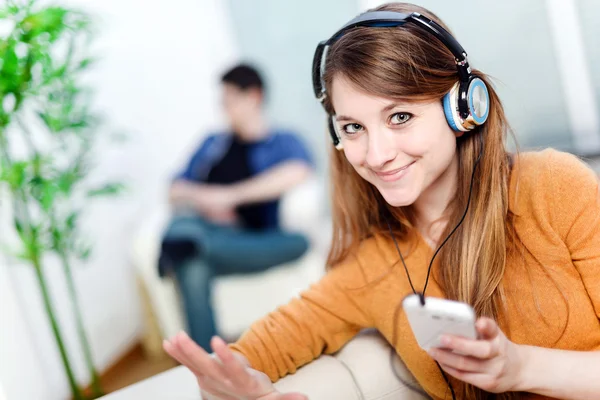 Beautiful blond listening to some music while her boyfriend is bored — Stock Photo, Image