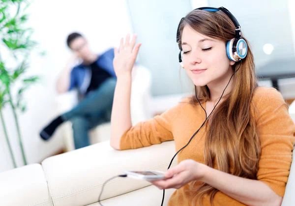 Beautiful blond listening to some music while her boyfriend is bored — Stock Photo, Image