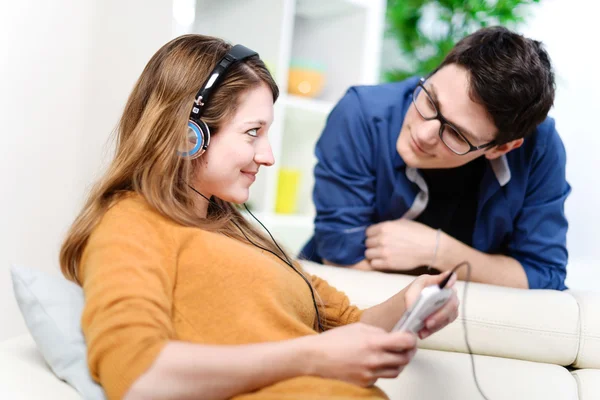 Hermosa rubia escuchando música mientras su novio la mira con amor —  Fotos de Stock