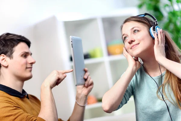 Vacker kvinna lyssnar på musik med hennes hörlurar medan hennes man tar bilder med en tablett — Stockfoto