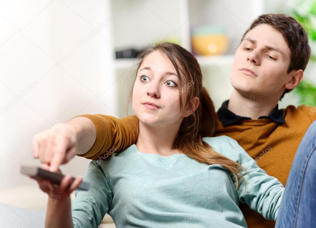 Beautiful woman and her husband trying to change tv channel on remote control