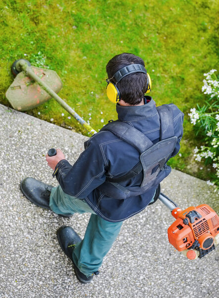 садовник с помощью веревочного триммера в парке
