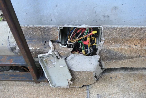 Kırık duvardaki bağlantı kutusunun içindeki açık elektrik kabloları, yüksek açı görüntüsü.   