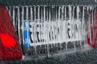 Ice-covered license plate with icicles, close up. Icing vehicle on a winter day after freezing rain in Ukraine. Blurred background.
