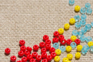 Renkli boncuklar tekstil arka planına saçılmış. Yazıt için form alın. Dekoratif parlak elementler. Boşluğu kopyala, üst görünüm.