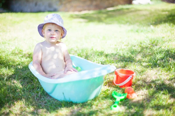 Liten flicka leker med vattnet på gräset — Stockfoto