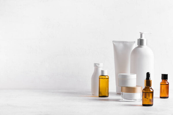 Косметические средства для кожи на белом столе, ассортимент косметических бутылок, здоровая косметология, концепция санаторно-курортного лечения, копировальное пространство.
