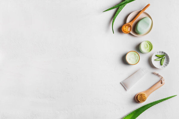 Aloe vera plant leaves, gel, skin care products on white, top view, copy space. Natural organic aloe vera cosmetics for face, hair and body care.