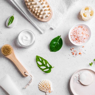 Beyaz taş zemin, yeşil yapraklar, deniz tuzu, kozmetik kremi ve masaj fırçası üzerine kaplıca ve cilt bakımı kavramı..