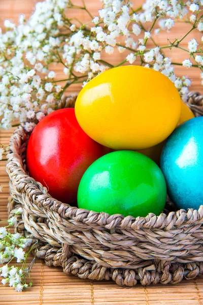 Colored painted eggs in a wattled basket with flowers — Stock Photo, Image