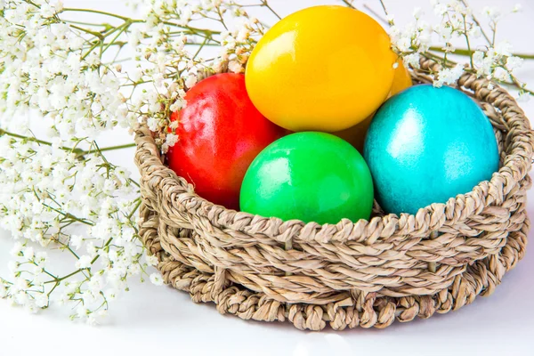 Colored painted eggs in a wattled basket with flowers — Stock Photo, Image