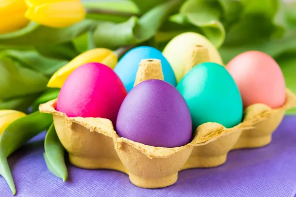 Colorful easter eggs in packing box with tulips flowers — Stock Photo, Image