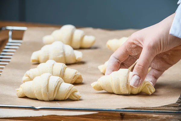 The cook puts croissants on a baking sheet on the table with ingredients