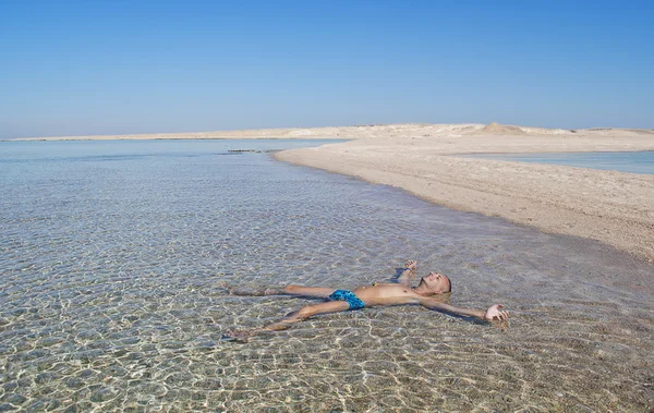 Ocio, placer. Egipto, Mar Rojo. Arena, isla desierta. Un hombre toma el sol acostado en el agua . — Foto de Stock