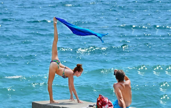 Красивая женщина рядом с морем перед мужчиной, делающим шпагат — стоковое фото