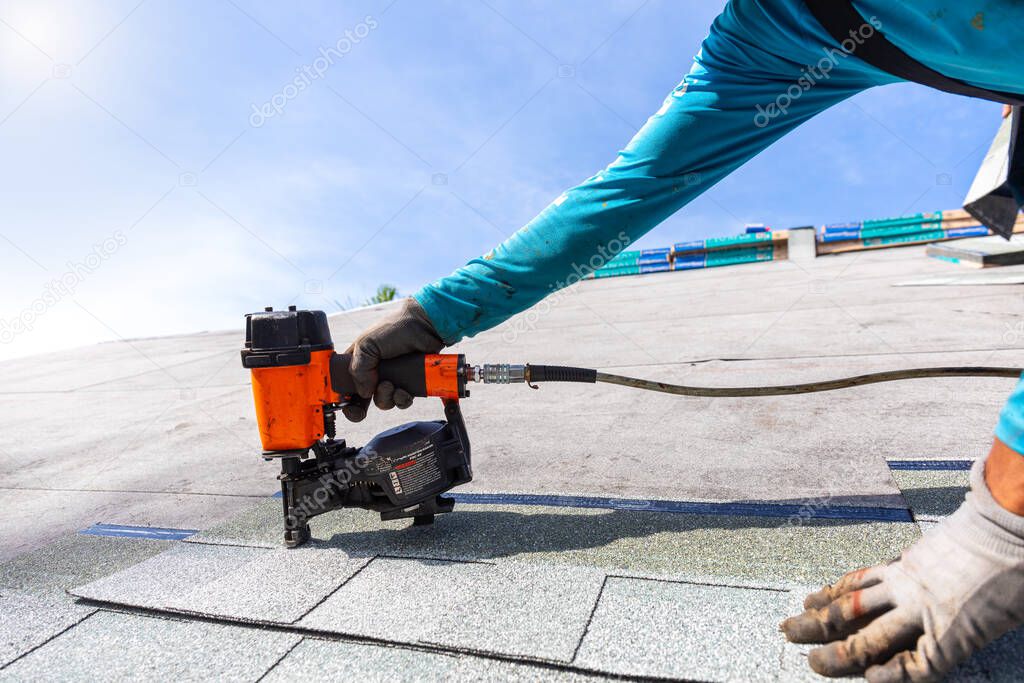 roofer installing roof shingles with pneumatic roofing nailer.