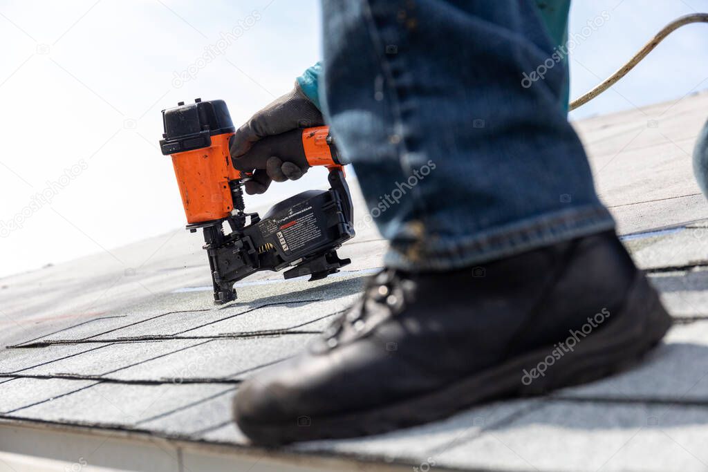 roofer installing roof shingles with pneumatic roofing nailer.