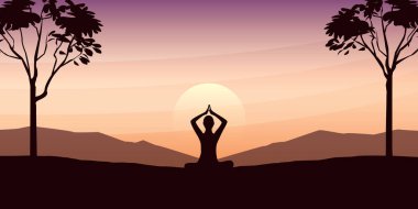 Yogada arabuluculuk yapan kişi, gün batımında büyük ağaçlar ve dağ manzaralı güzel bir manzara üzerinde poz verir.