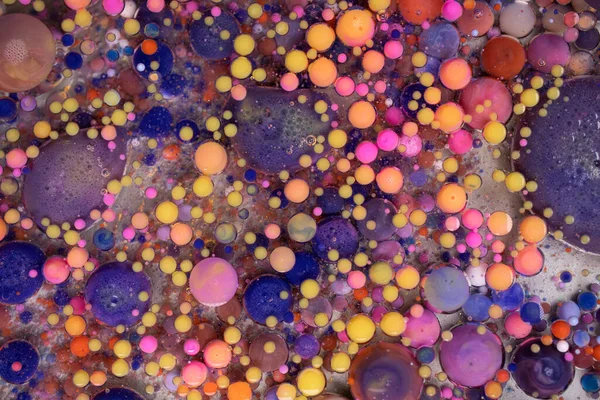 Purple, blue, pink and yellow liquids mix. Creative multicolor background. Acrylic paint balls abstract texture. Bright colors fluid, flowing wallpaper design. Mixed pigments violet backdrop.