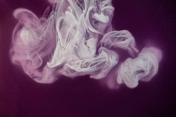 Real shot color paint drops in water. Abstract white Ink cloud collision isolated on violet background. Liquid marble pattern. Modern art. Abstract fluid acrylic painting.