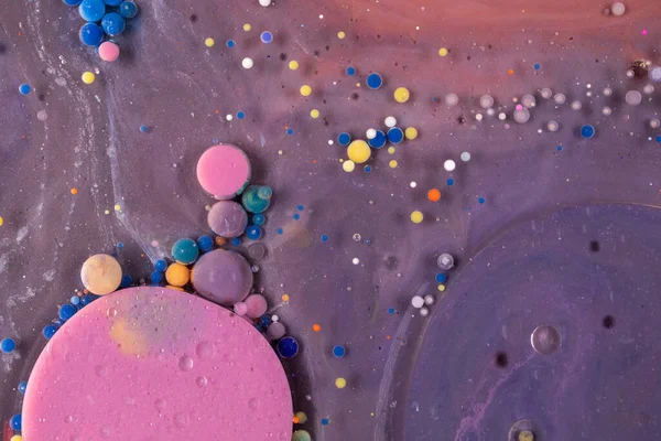 Purple, blue, pink and yellow liquids mix. Creative multicolor background. Acrylic paint balls abstract texture. Bright colors fluid, flowing wallpaper design. Mixed pigments violet backdrop.