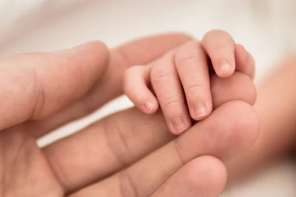 Recién nacidos mano pequeña sostiene los dedos de su padre cariñoso — Foto de Stock