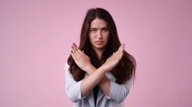 4k video of a serious young woman standing with hands crossed over pink background. Stop concept.