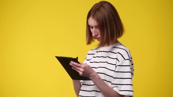 Vídeo Una Mujer Concentrada Escribiendo Algo Aislado Sobre Fondo Amarillo — Vídeos de Stock