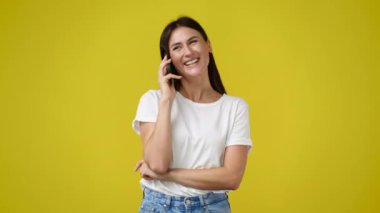 Sarı arka planda, telefonda konuşan hoş bir kadının 4K videosu. Teknoloji kavramı.