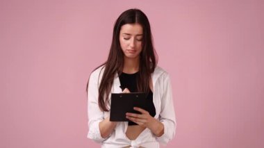 Pembe arka planda izole edilmiş bir şeyi yazan konsantre bir kadının 4k videosu. Yazma kavramı,